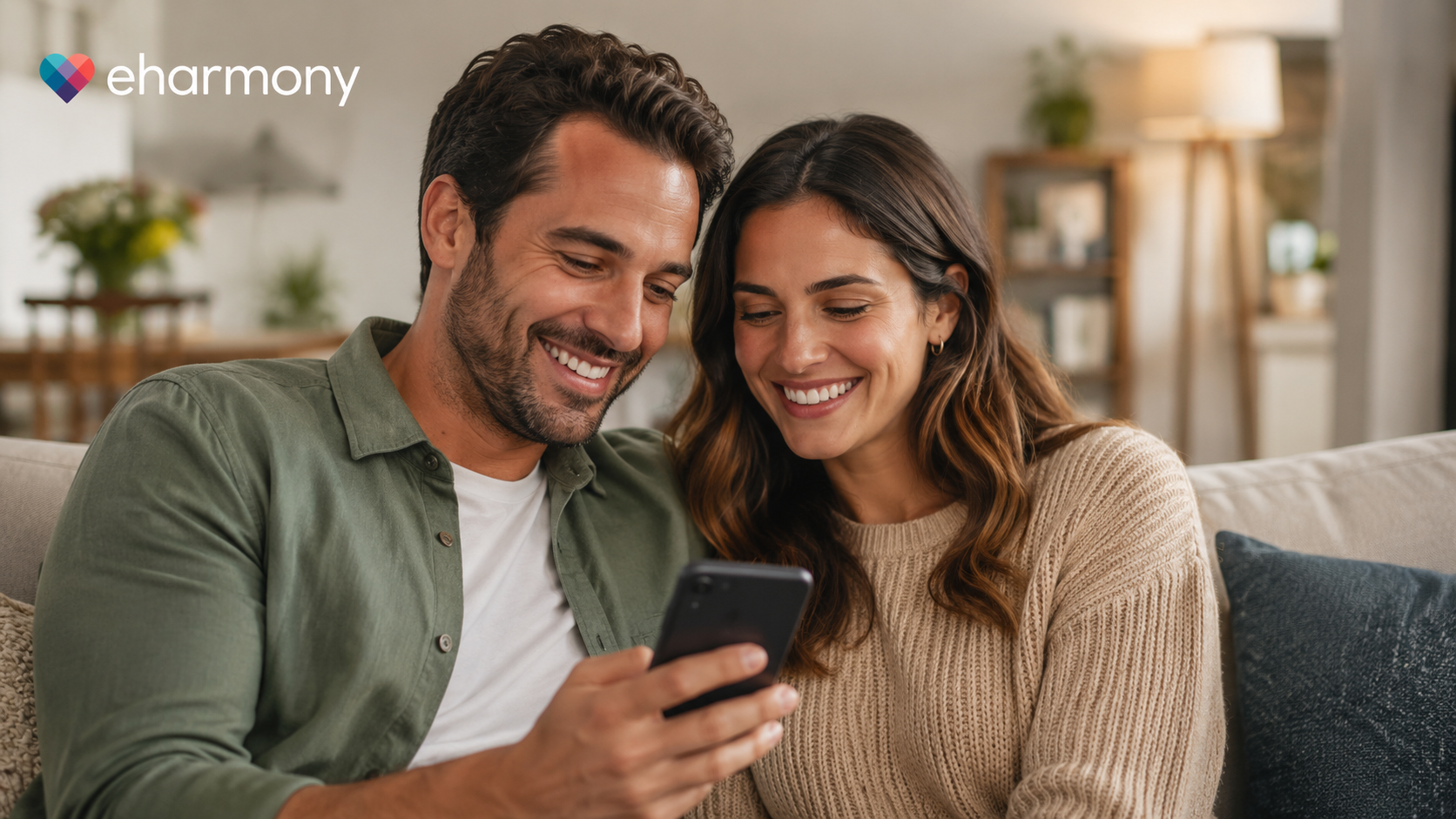 Happy couple smiling while using the eHarmony dating app on a smartphone at home, representing online dating for serious relationships and long-term compatibility.