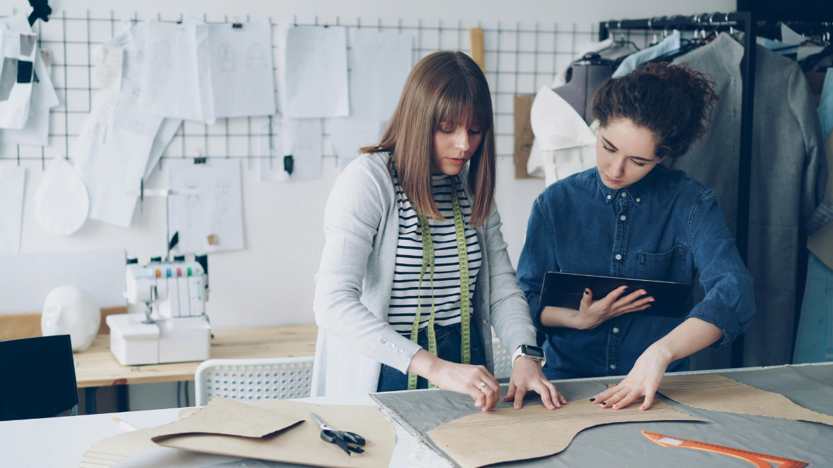 Fashion designers reviewing clothing patterns and fabric samples at a worktable in a design studio.