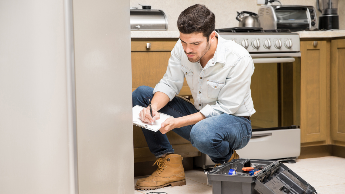 Handyman repair professional inspecting a kitchen appliance with tools during a home repair service.