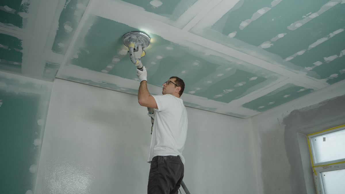 Handyman sanding and smoothing a drywall ceiling during an indoor home repair and renovation project.